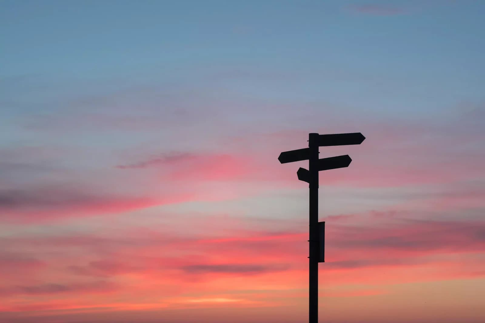 Un cartello con più direzioni, in controluce su un cielo al tramonto